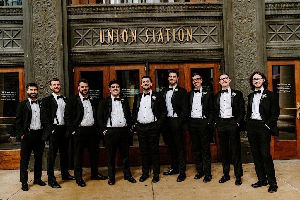 A groom stands with his 8 groomsmen for a portrait photo outside the front entrance of Chicago's Union Station