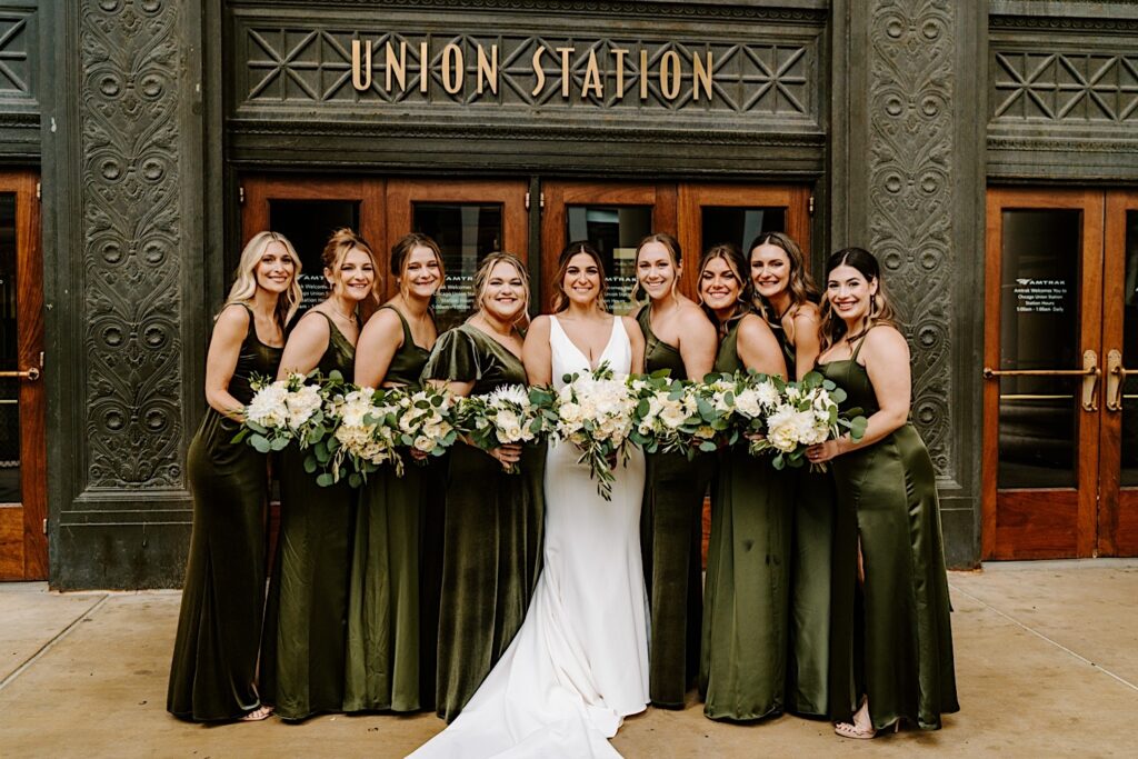 A bride stands with her 8 bridesmaids on either side of her for a portrait photo outside the entrance of Chicago's Union Station