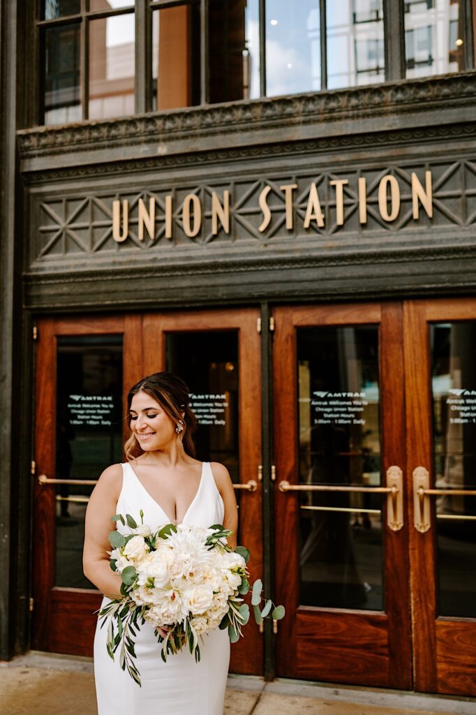 A bride looks down while holding her bouquet towards the camera as she stands in front of the entrance of Chicago's Union Station