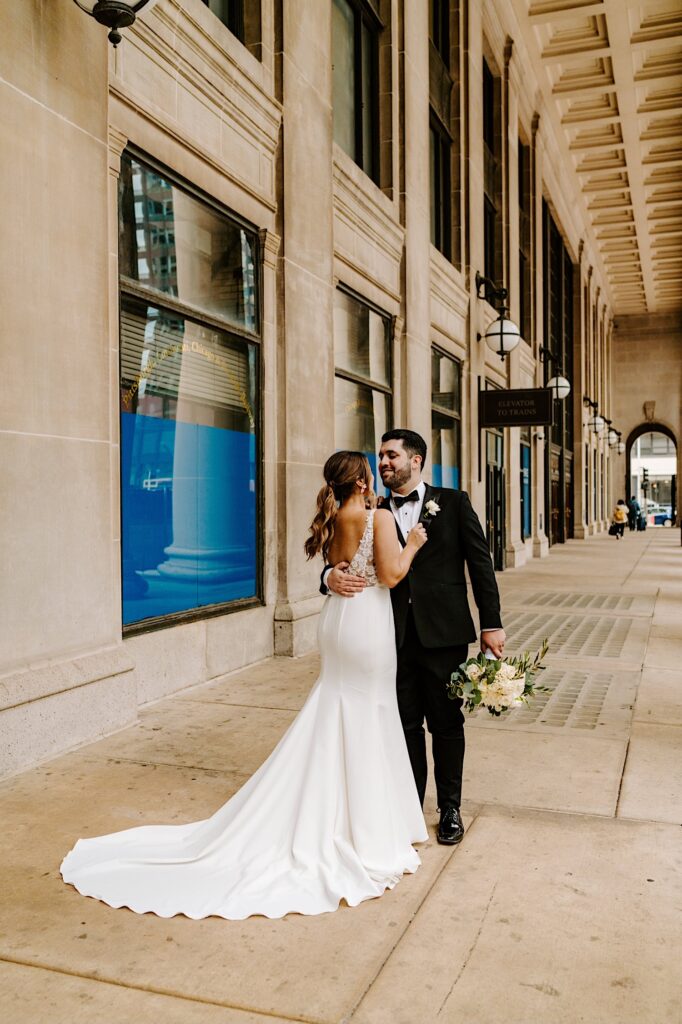 A bride and groom smile at one another while they embrace outside of Chicago's Union Station