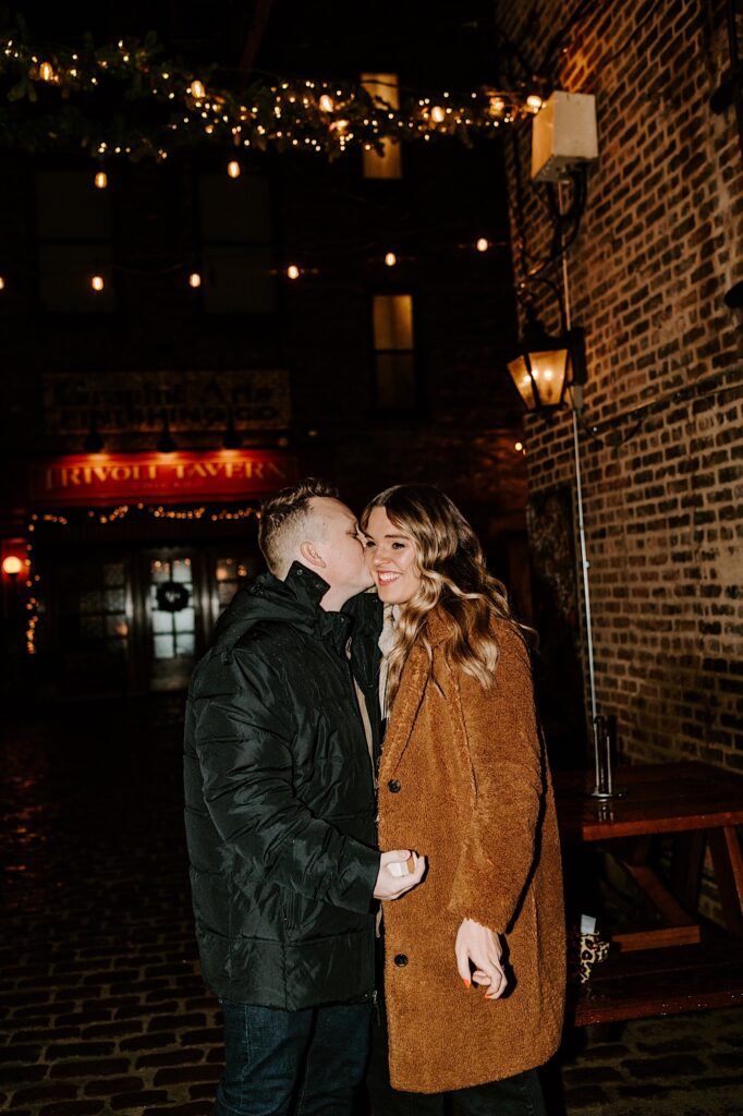 A woman smiles as a man kisses her cheek while outside of Trivoli Tavern in Chicago after her proposed to her