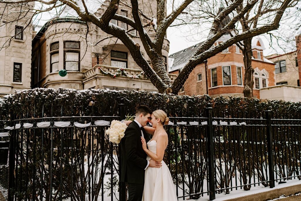 A bride and groom smile at one another while embracing outside of their Chicago apartment as it snows around them