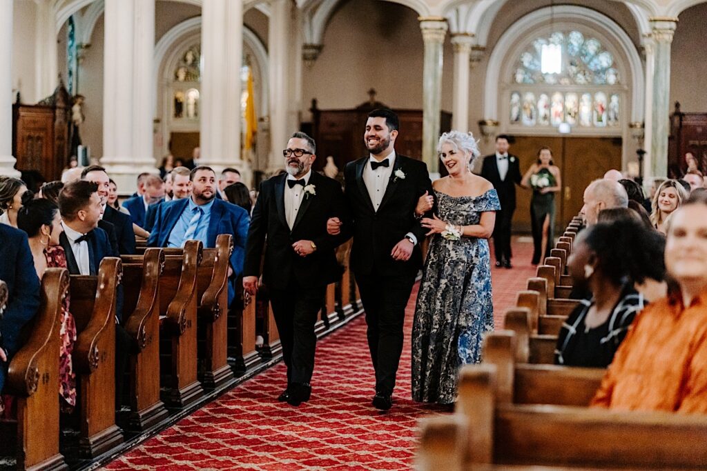 A groom walks down the aisle of St Michael Church in Chicago with his parents for the start of his wedding ceremony