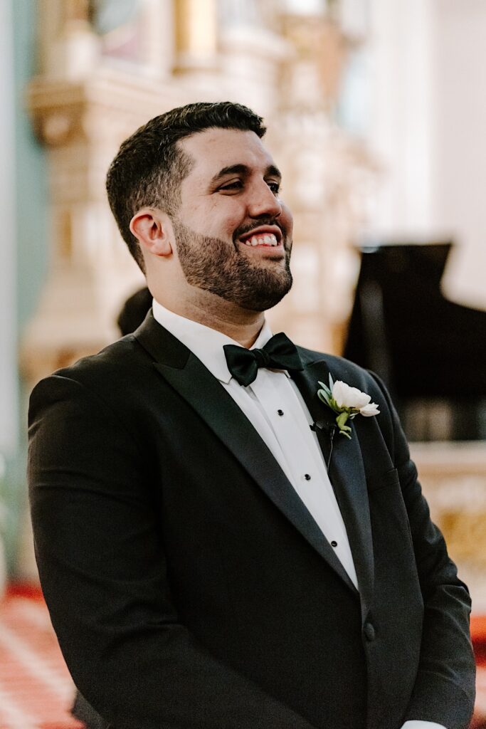 A groom smiles as he stands inside of St Michael Church in Chicago as the bride is walked down the aisle