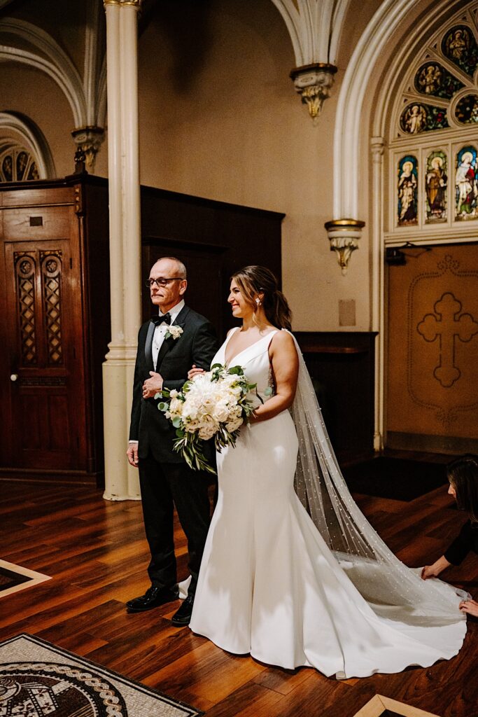 A bride smiles as her father begins to walk her down the aisle for her wedding ceremony at St Michael Church in Chicago