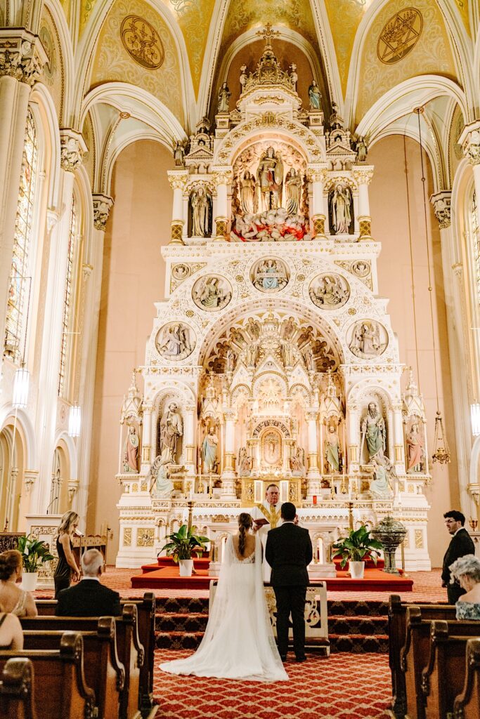 A bride and groom stand side by side at the altar of St Michael Church in Chicago as the pastor speaks for their wedding ceremony