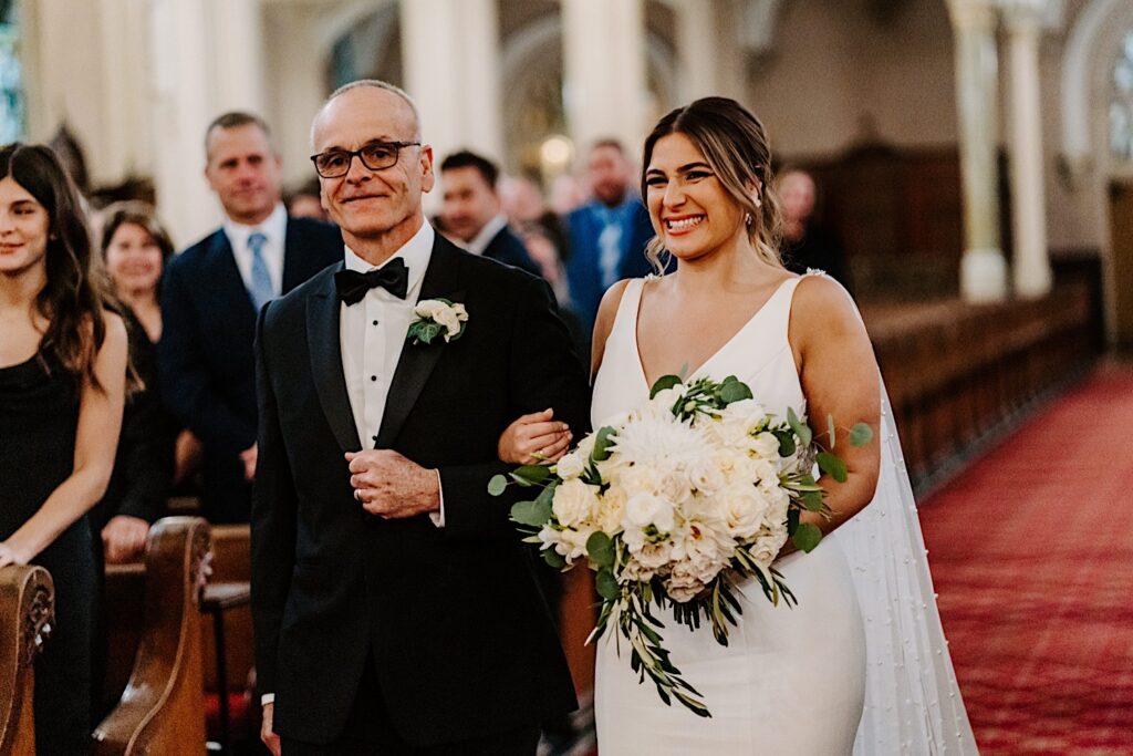 A bride smiles as her father walks her down the aisle of St Michael Church in Chicago for her wedding ceremony