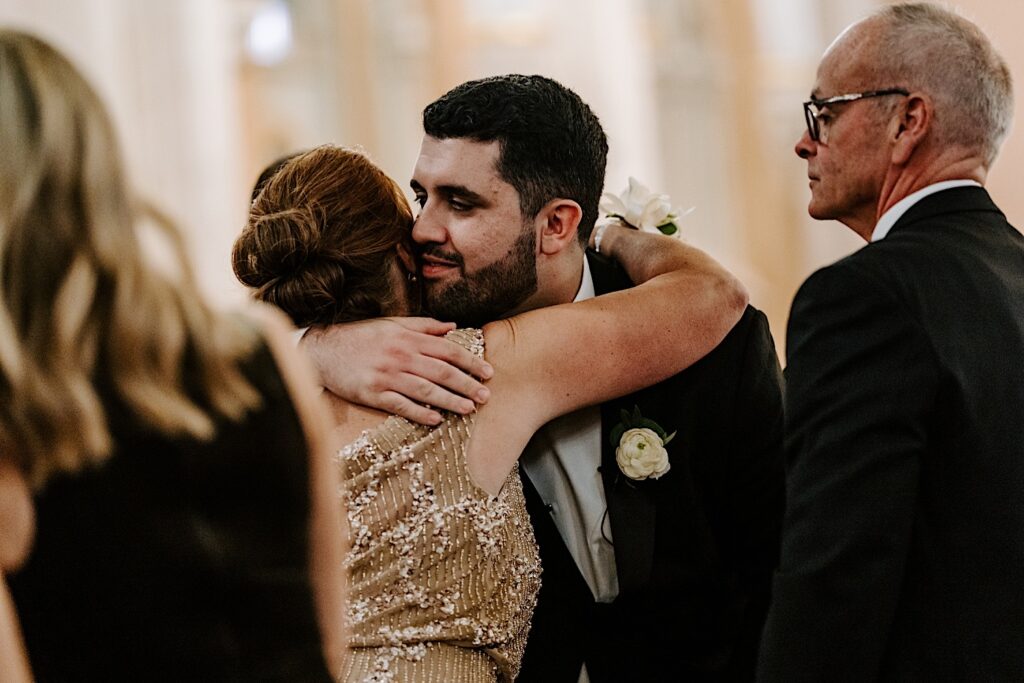 A groom hugs the mother of the bride while inside of St Michael Church in Chicago after their wedding ceremony