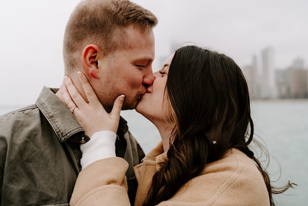 A couple kiss one another while having their engagement photos taken on a cloudy day at North Avenue Beach in Chicago