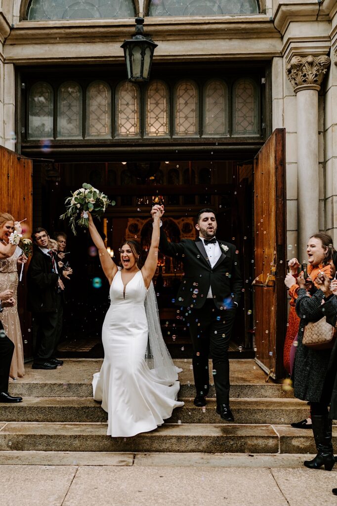 A bride and groom exclaim in excitement as they exit St Michael Church in Chicago after their wedding ceremony, guests around them blow bubbles in the air