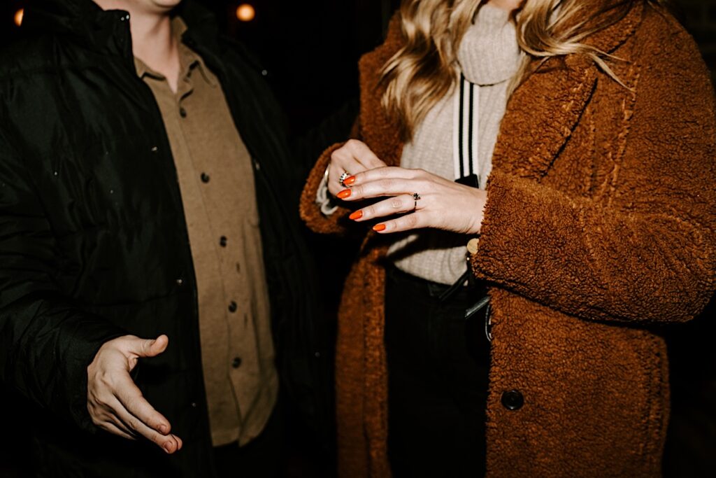 Close up photo of a woman's hand with an engagement ring on it and a man standing next to her, the photo was taken after their surprise proposal in Chicago's West Loop