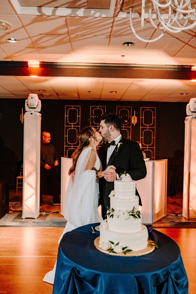 A bride and groom kiss one another while standing next to their wedding cake during their reception at the Voco Hotel in Chicago