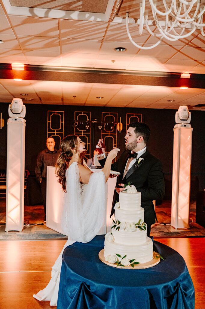 A bride and groom feed each other a piece of their wedding cake during their reception inside the Voco Hotel