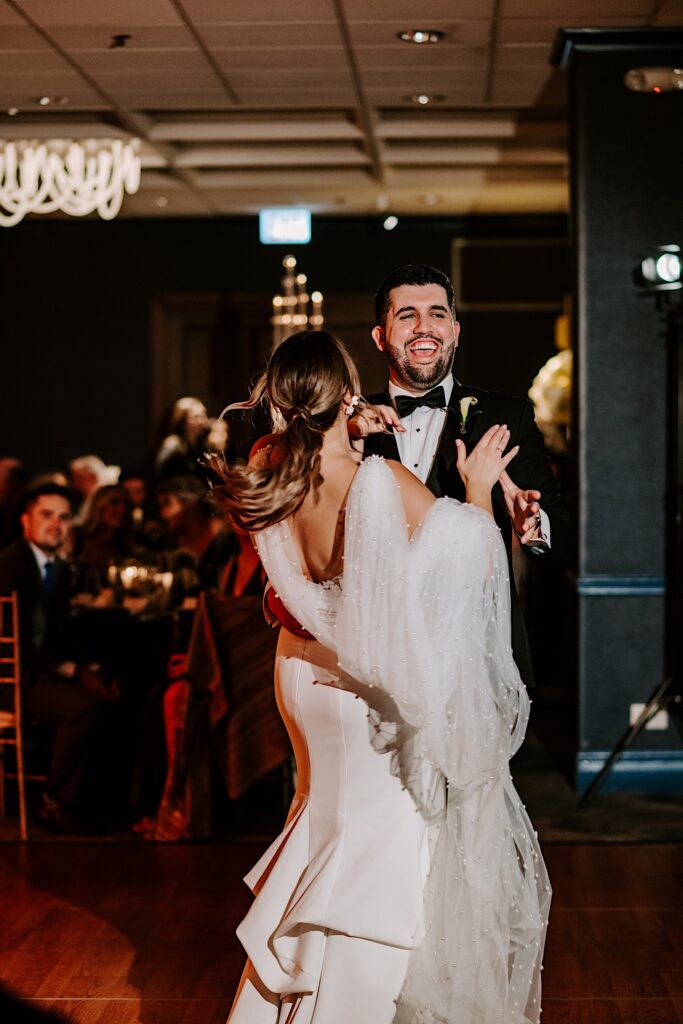 A groom smiles and laughs while dancing with the bride during their reception inside the Voco Hotel in Chicago