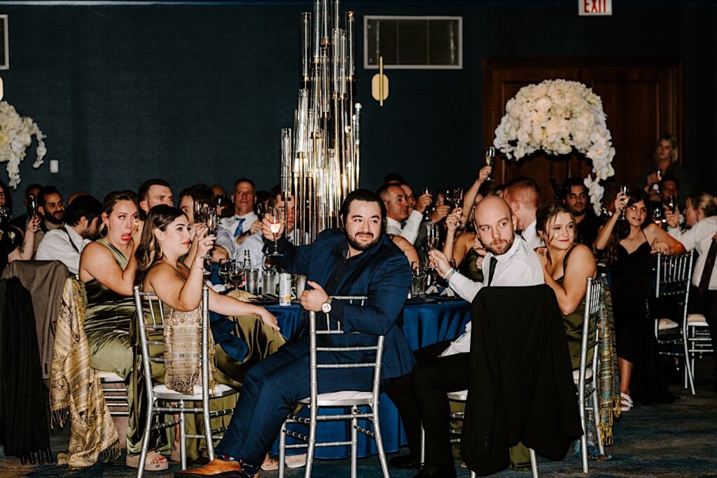 Guests of a wedding reception at the Voco Hotel in Chicago sit and raise their glasses for a toast during a speech