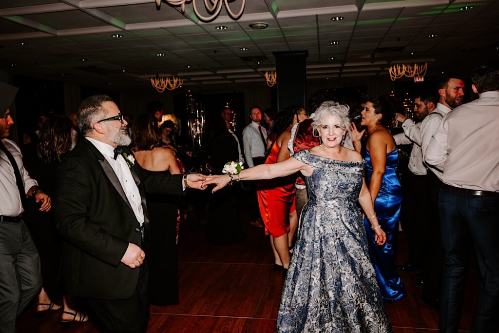 The mother of the groom smiles at the camera while dancing with her husband and other guests during a wedding reception at the Voco Hotel in Chicago