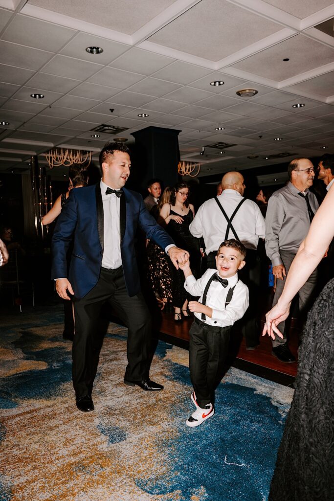 A young boy dances with his father alongside other guests of a wedding reception at the Voco Hotel