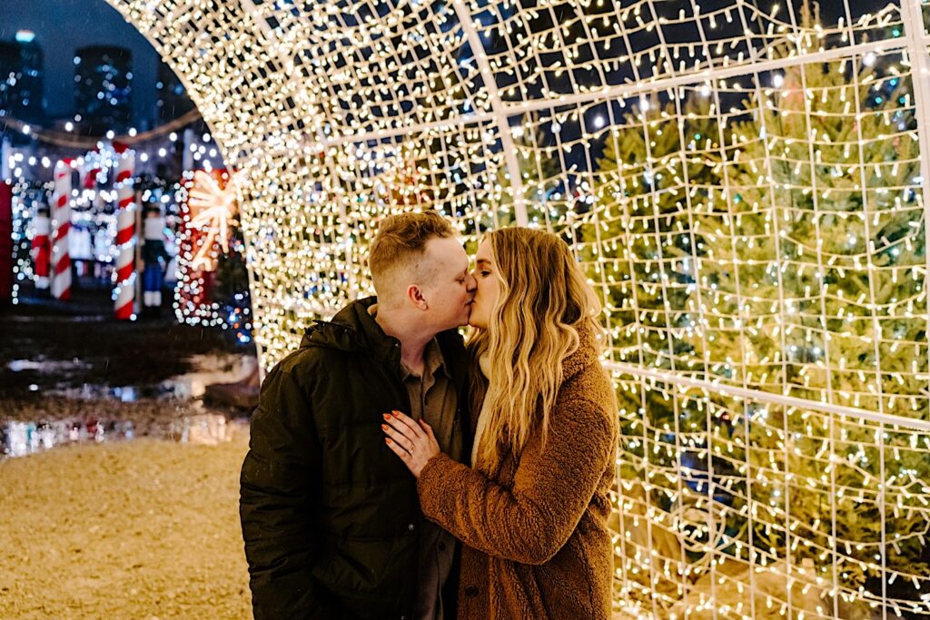 A couple kiss one another while under a tunnel of lights in the Jack Frost Market to celebrate their proposal in Chicago's West Loop