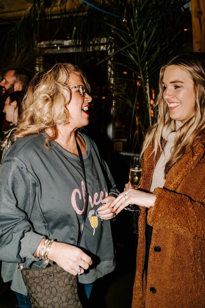 A woman shows off her engagement ring to her mother while sipping champagne in a bar after she was proposed to.