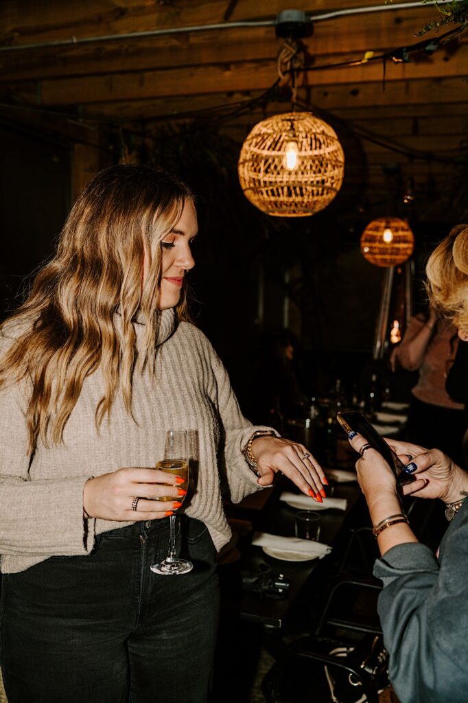 A woman shows off her engagement ring to a woman who takes a picture on her phone while inside of a Chicago bar