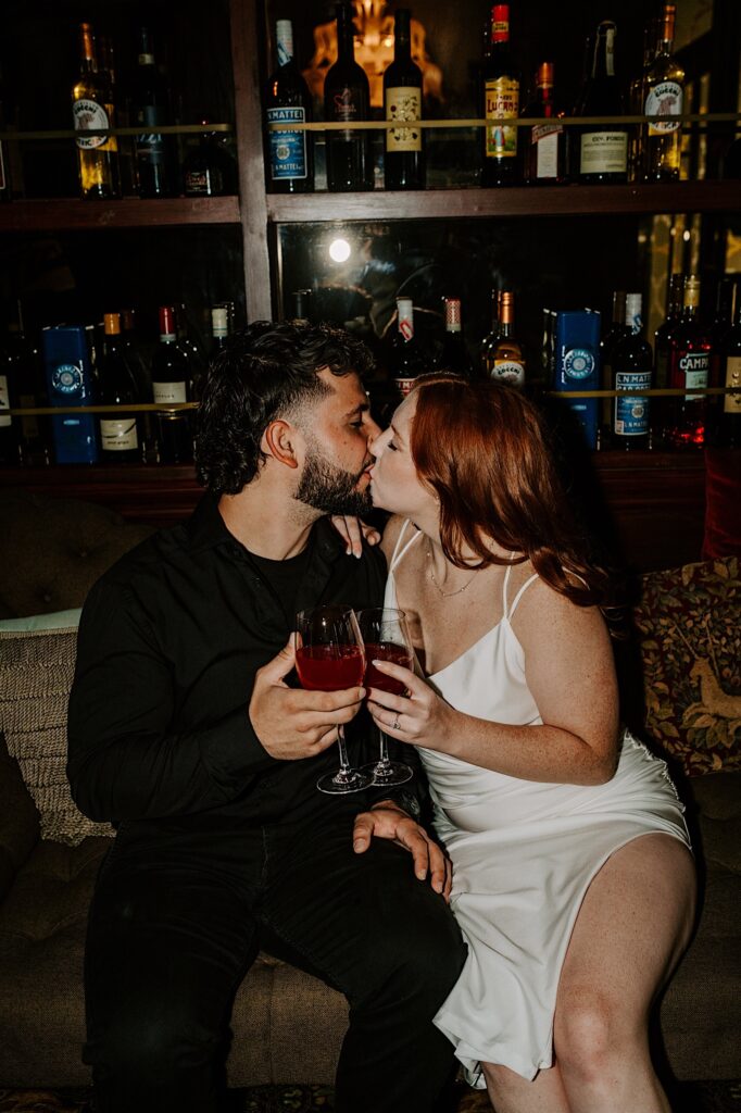A couple kiss while sitting on a couch together in a Chicago bar as they drink wine