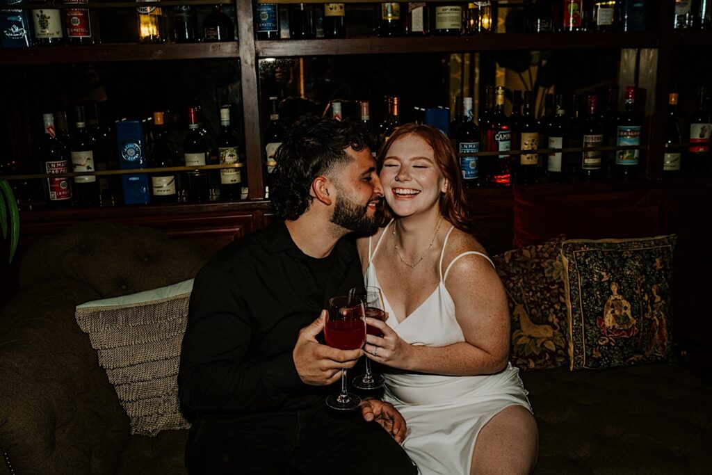 A woman smiles as a man touches her cheek with his nose while they sit on a couch in a Chicago bar together