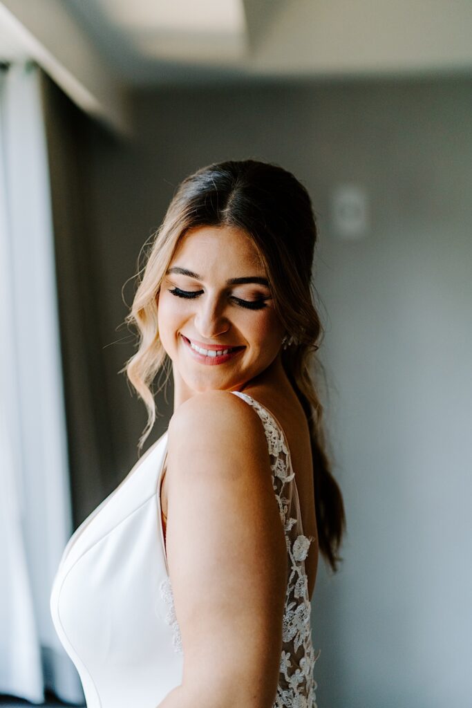 A bride smiles over her shoulder while looking down towards the back of her wedding dress