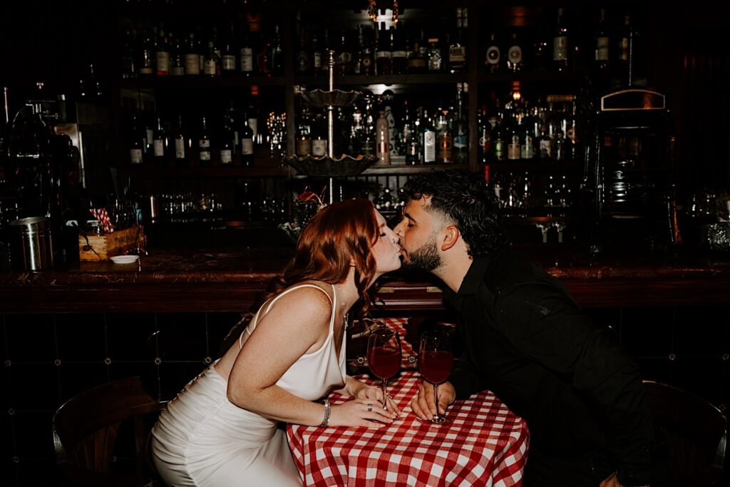 A couple lean over a table to kiss one another while in a Chicago bar