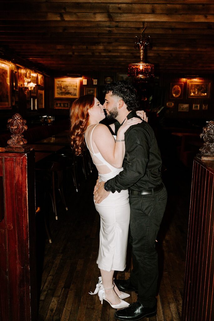 A couple kiss and embrace while standing in a Chicago bar