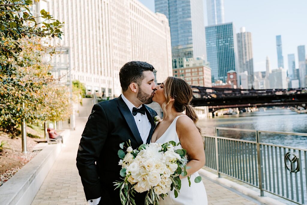 A bride and groom kiss one another while standing next to the Chicago River, which is right next to their wedding venue, the Voco Hotel