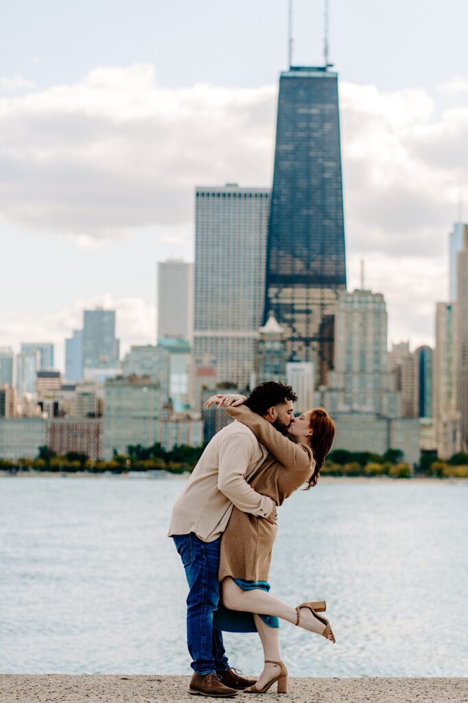 A couple kiss one another while standing in front of Lake Michigan and the Chicago skyline