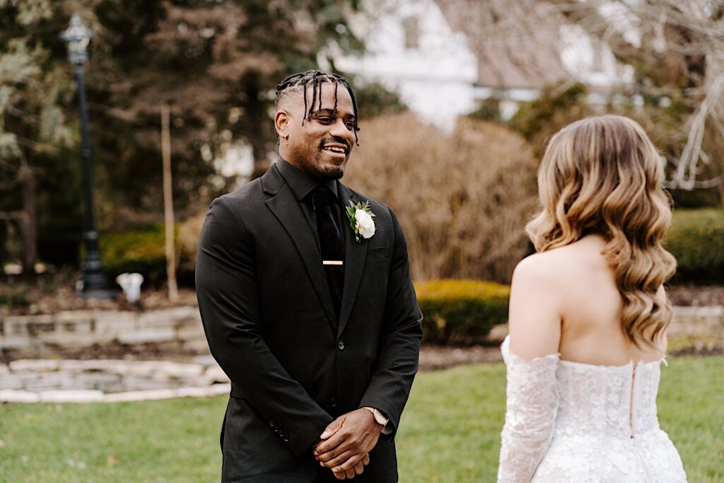 A groom smiles as he sees the bride in her wedding dress for the first time during their first look outside of The Haley Mansion
