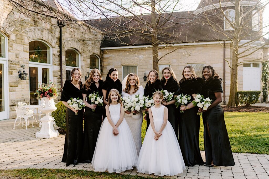 A bride stands with her 7 bridesmaids and 2 flower girls while taking wedding party photos outside of The Haley Mansion