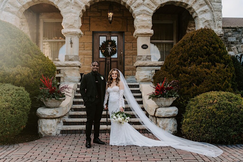 A bride and groom pose for a portrait photo in front of a set of stairs outside of their wedding venue, The Haley Mansion