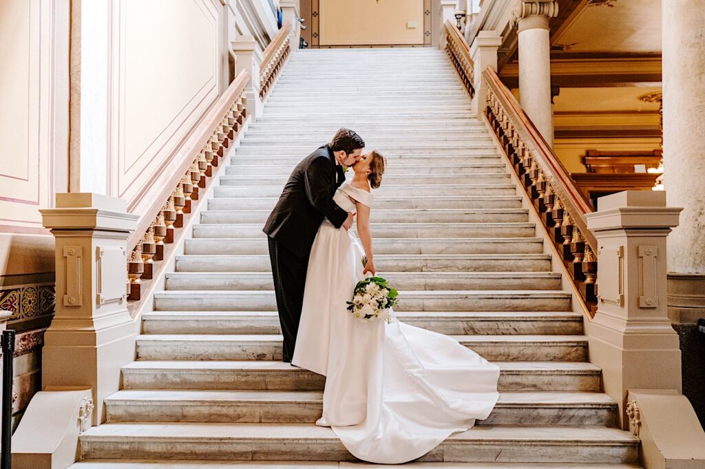 A bride and groom kiss one another while standing on a marble staircase