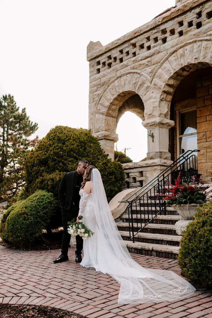 A bride and groom kiss one another while standing in front of a set of stairs of The Haley Mansion