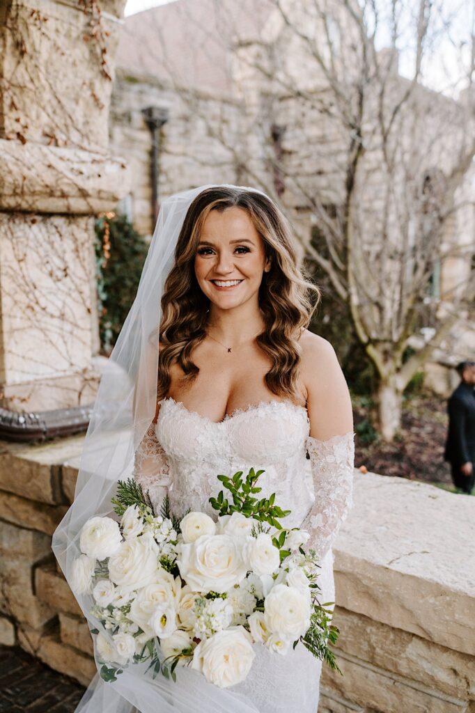 A bride smiles at the camera while standing on a stone balcony of The Haley Mansion
