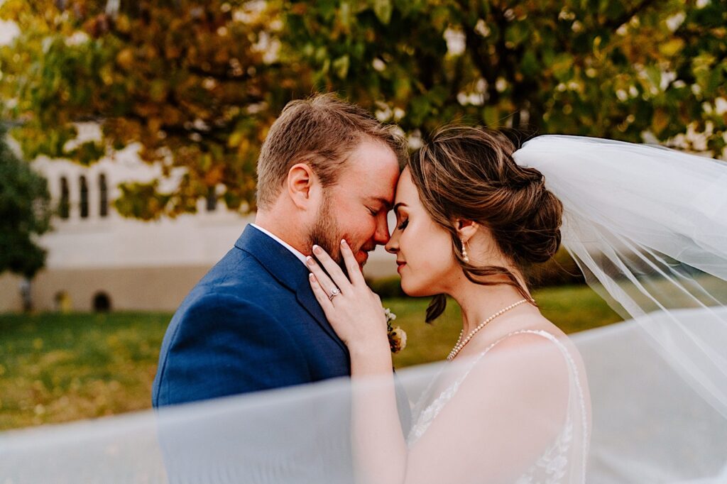 A bride and groom embrace with their eyes closed for a wedding day portrait outdoors