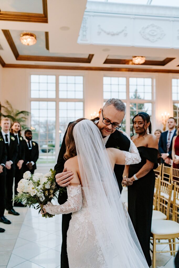 A bride hugs her father after he escorted her down the aisle for her ceremony at The Haley Mansion