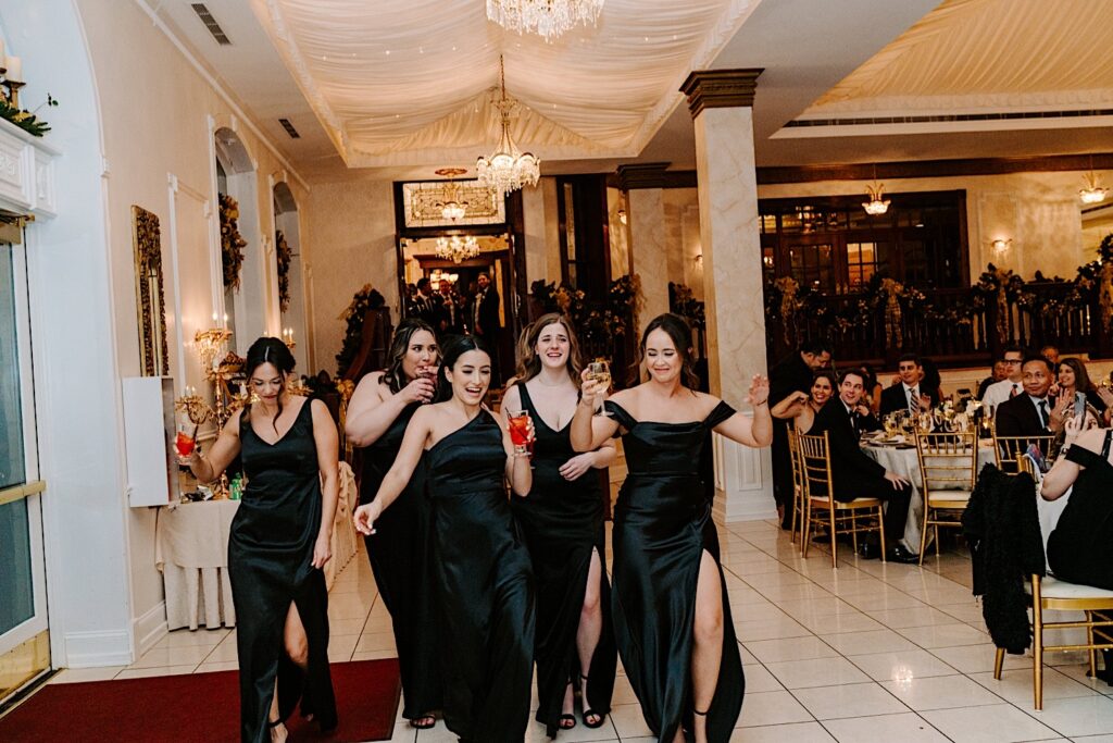 Bridesmaids enter an indoor wedding reception at The Haley Mansion together as they dance and laugh