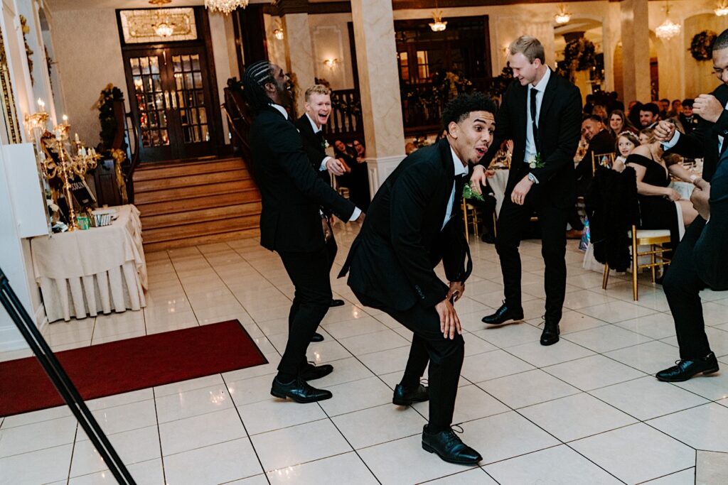 Groomsmen enter an indoor wedding reception at The Haley Mansion together dancing and laughing