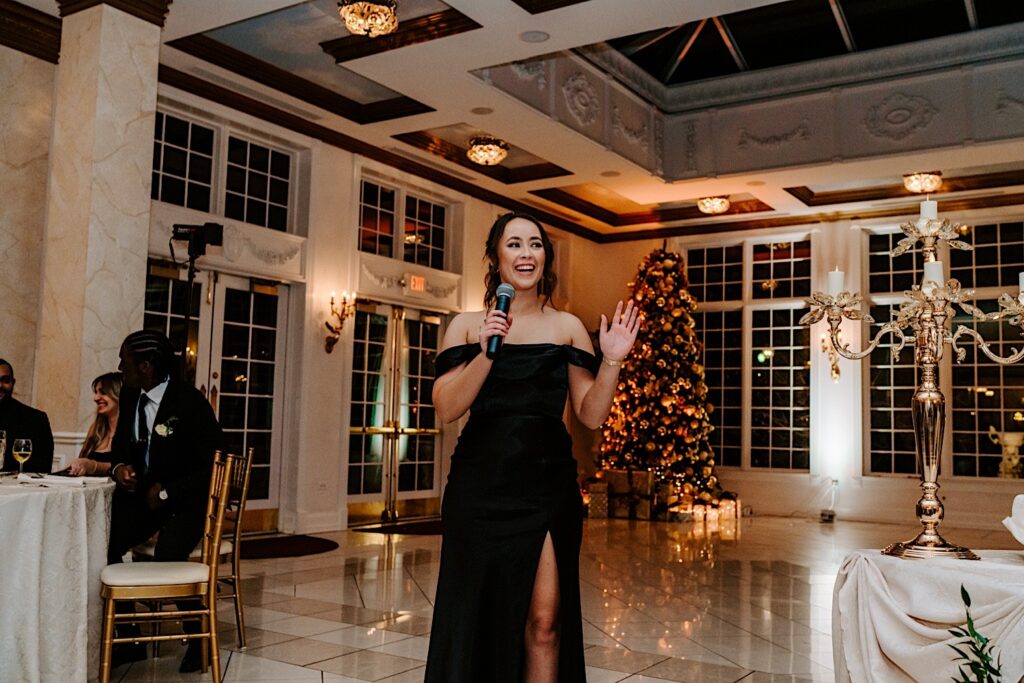 A bridesmaid stands while giving a speech during an indoor wedding reception at The Haley Mansion