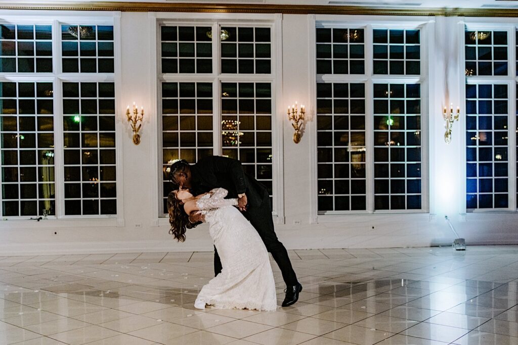 A bride and groom kiss one another while the bride is being dipped during the first dance of their indoor wedding reception at The Haley Mansion