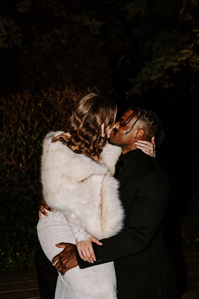 A bride and groom kiss one another while outside for some late night wedding portraits