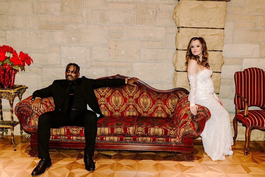 A bride and groom pose for a portrait photo with a regal couch in The Haley Mansion during their wedding reception