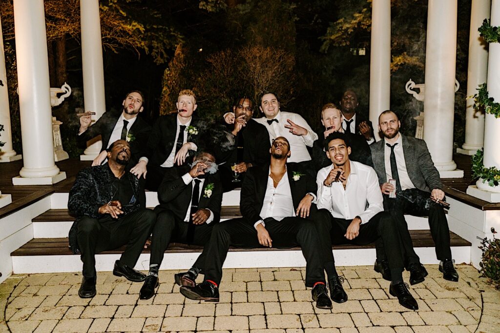 A groom smokes cigars with his groomsmen while outside of The Haley Mansion during his wedding reception