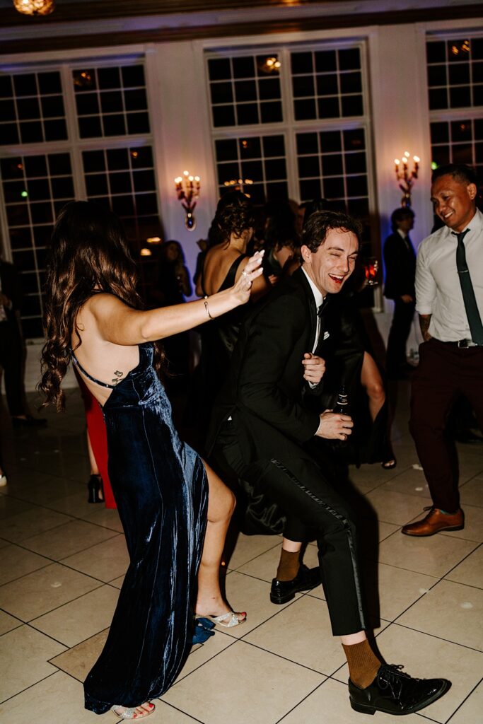 Guests of a wedding reception dance together as they smile and laugh
