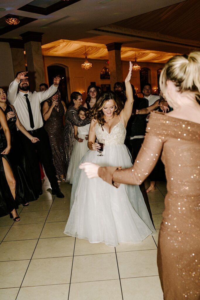 A bride enters the dance floor as guests cheer around her during her indoor reception