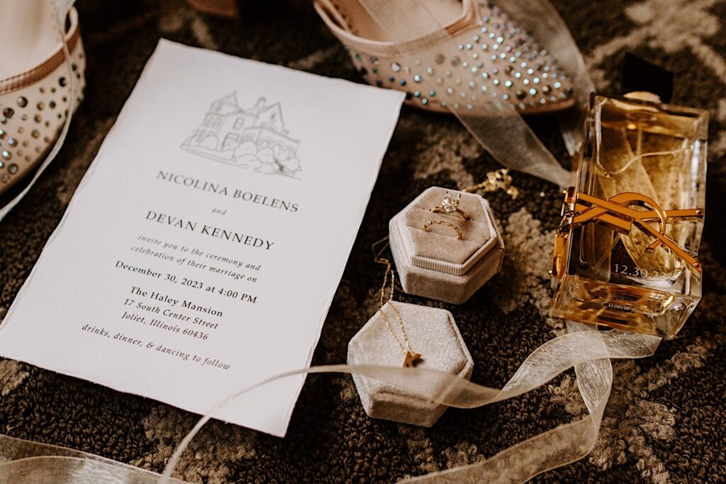 A wedding day flatlay consisting of invites, wedding rings, shoes, and perfume