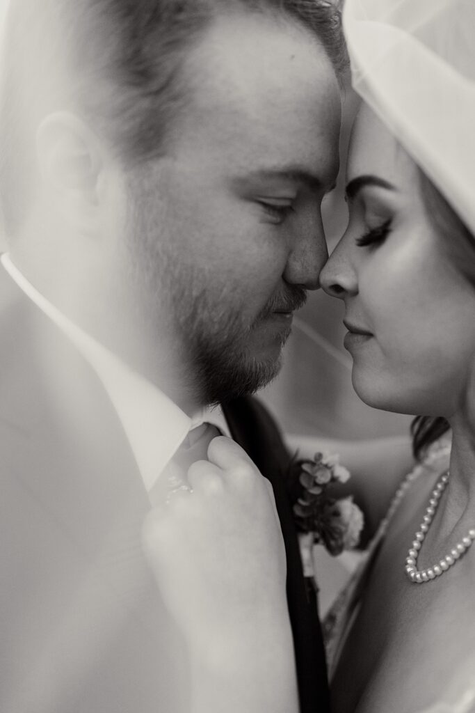 Black and white photo of a bride and groom about to kiss while under the bride's veil